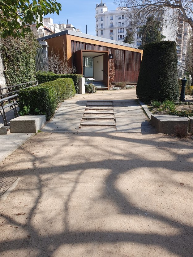 Rampa con acceso al edificio de la cafetería del jardín, con la estructura en tonos marrones