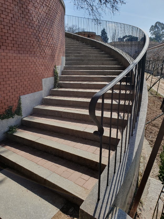 Inicio de las escaleras desde cerca, con una barandilla negra 