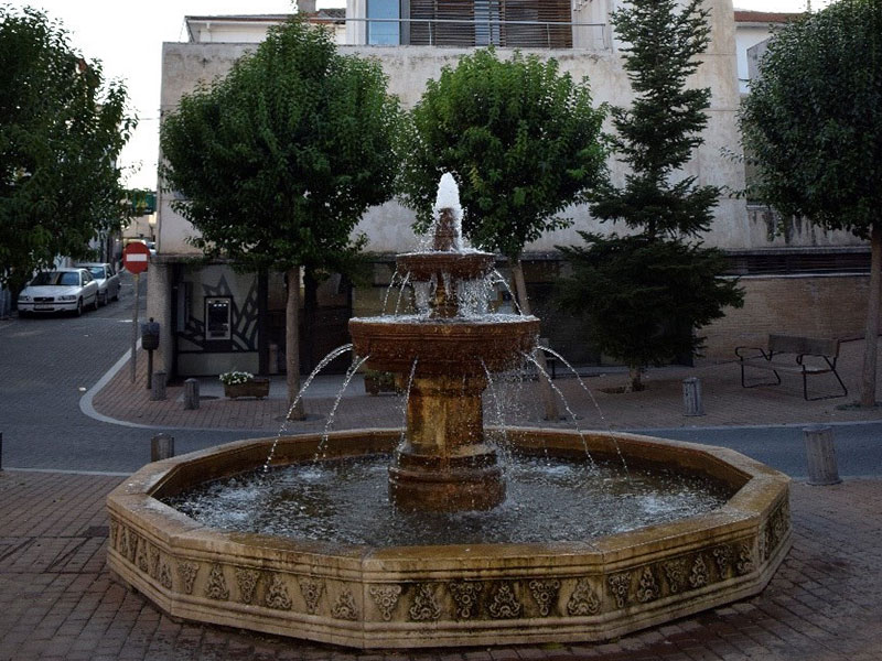 Basin fountain in the shape of a dodecahedron, made of stone and decorated with plant motifs. The water spout is a central pillar with two hemispherical bowls that pour the water through several spouts.