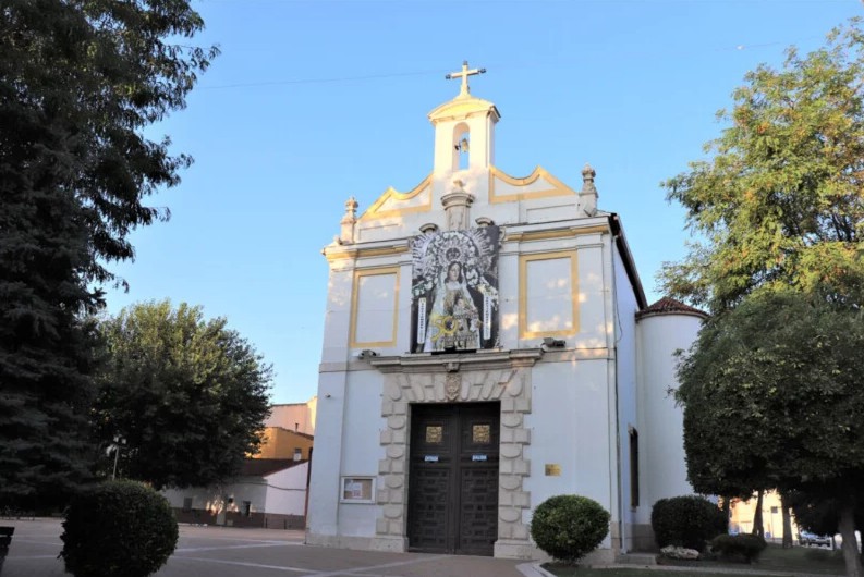 fachada de sobrio estilo barroco con elementos de arquitectura clásica lacada en blanco con pequeños detalles en tonos amarillos y una puerta central de madera, situada a las afueras del municipio.