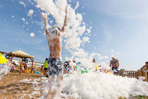 Imagen de niños jugando con la espuma en la playa.