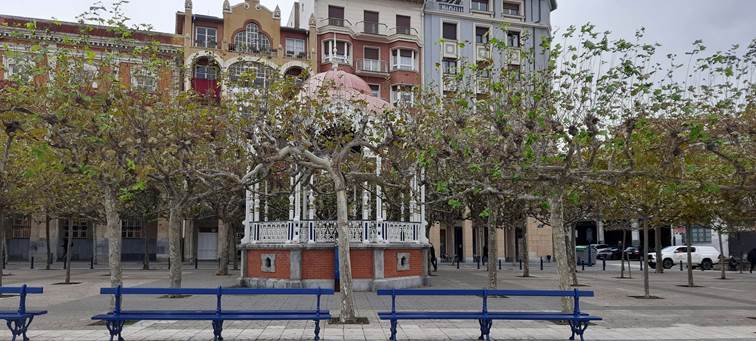 Kiosco de música en una plaza con bancos antiguos cubierta de plátanos trasmochados.