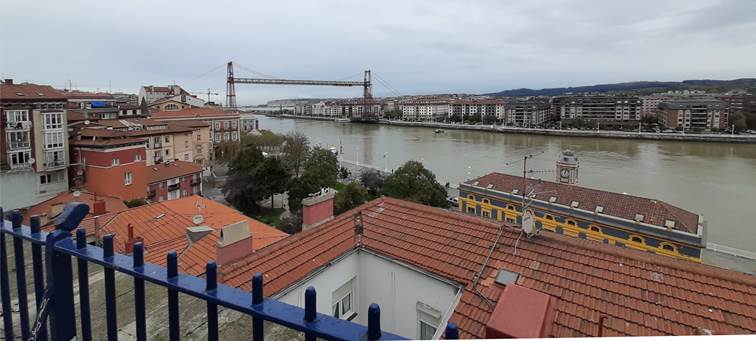 Itsasadarraren bokaleko ikuspegi panoramikoa, behean Portugaleteko eraikinak eta atzealdean Getxoko udalerria dituela, biak Bizkaiko Zubiak lotuta.