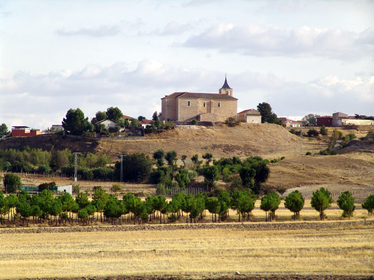 vista desde el exterior del municipio, donde destacan los campos cerealistas, de vides y olivos y la iglesia parroquial en el punto más alto.