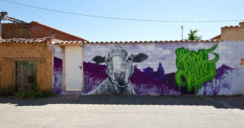 Fresque de moutons avec La Torre del Valle en arrière-plan dans des tons violets et le nom de la ville écrit en lettres vertes