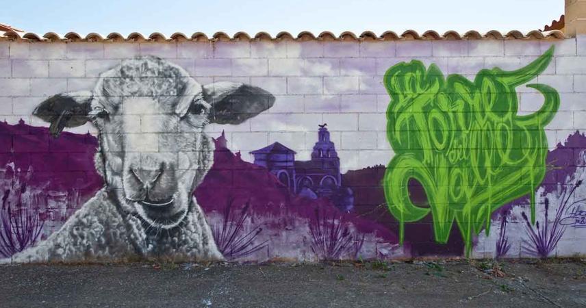 Fresque de moutons avec La Torre del Valle en arrière-plan dans des tons violets et le nom de la ville écrit en lettres vertes