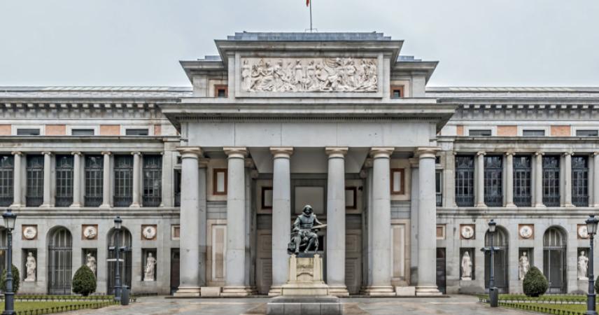 Photo de l'entrée principale du musée du Prado, la porte Velázquez. Face à l'entrée se trouve une sculpture de Diego Velázquez, un peintre sévillan qui s'est installé à la cour de Philippe IV et a produit des œuvres importantes, telles que Les Ménines, Les Hilanderas et plusieurs portraits de la famille royale, qui sont aujourd'hui conservés au musée.