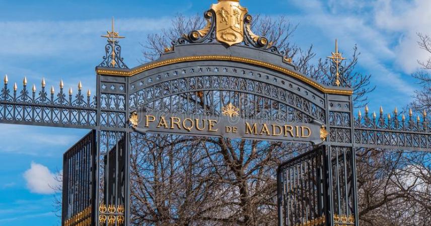Photo d'une des entrées du Parc. Il s'agit de la Puerta de España, formée de plusieurs entrées avec des portes à barreaux qui donnent accès au parc. Au dessus de l'arc de la porte principale, on peut voir les armoiries républicaines. Il convient également de noter la plaque, posée pour la première fois en 1893, qui mentionne le nouveau nom donné aux jardins : Parc de Madrid. 