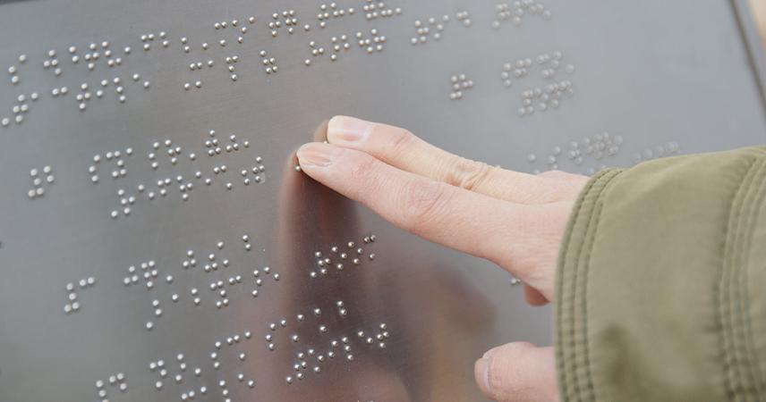 Los dedos de una persona tocando un texto braille en una placa